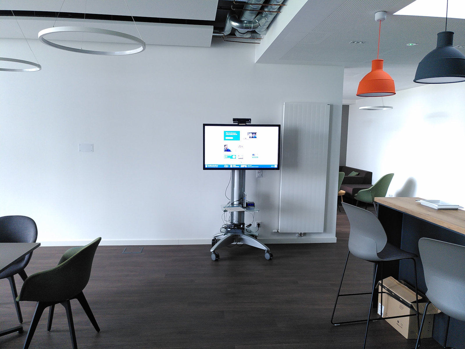 A cafeteria-style room with no people in it, with a large touch screen mounted on a stand visible near a door